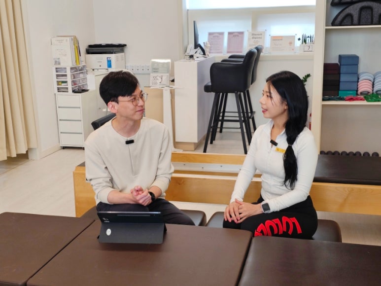 매직바디 교육장에서 강사와 교육생이 기구 옆에 마주 앉아 태블릿을 놓고 이야기를 나누는 모습