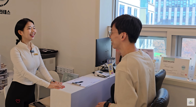 필라테스 센터 상담 데스크에서 강사가 회원을 맞이하며 이야기를 나누는 모습