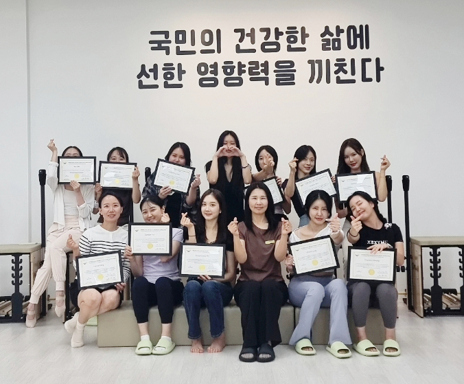 국민의 건강한 삶에 선한 영향력을 끼친다는 문구가 적힌 배너 앞에서 수료생들이 자격증을 들고 단체 기념사진을 찍는 모습